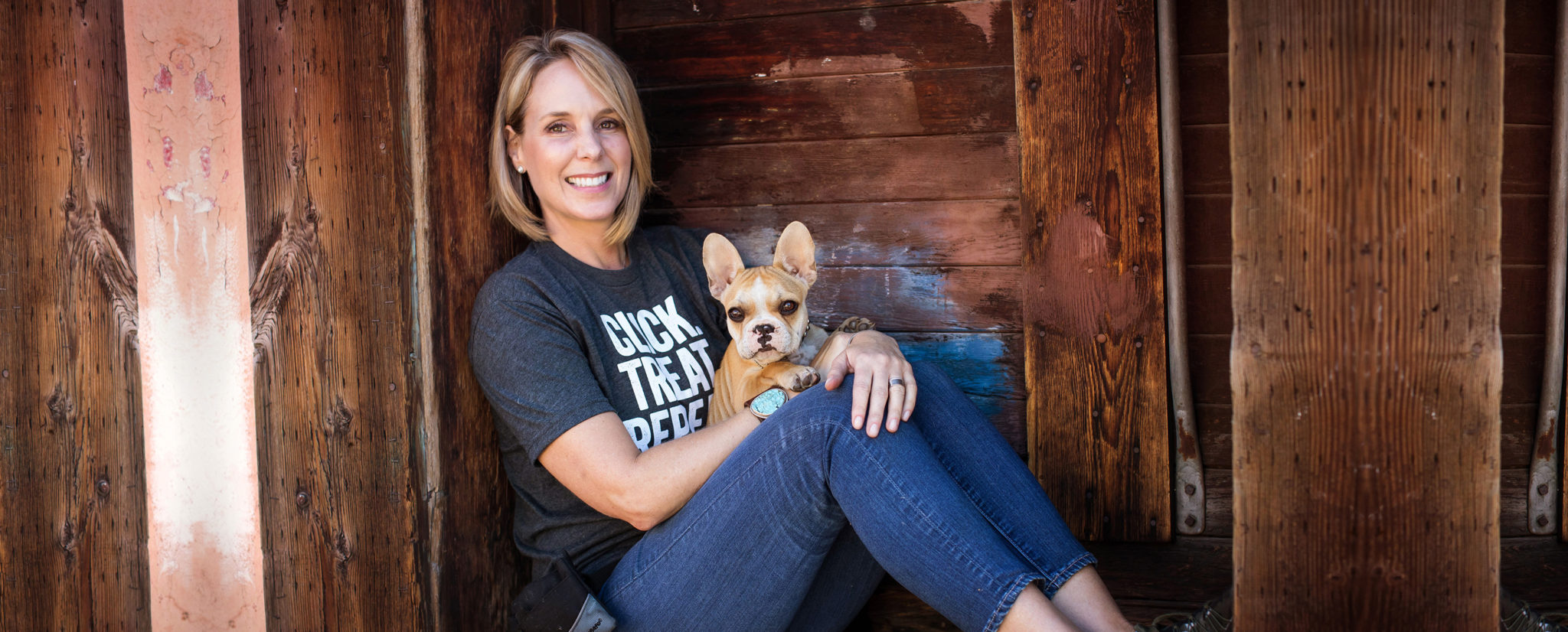 Tera sitting with a French bulldog against a wooden wall
